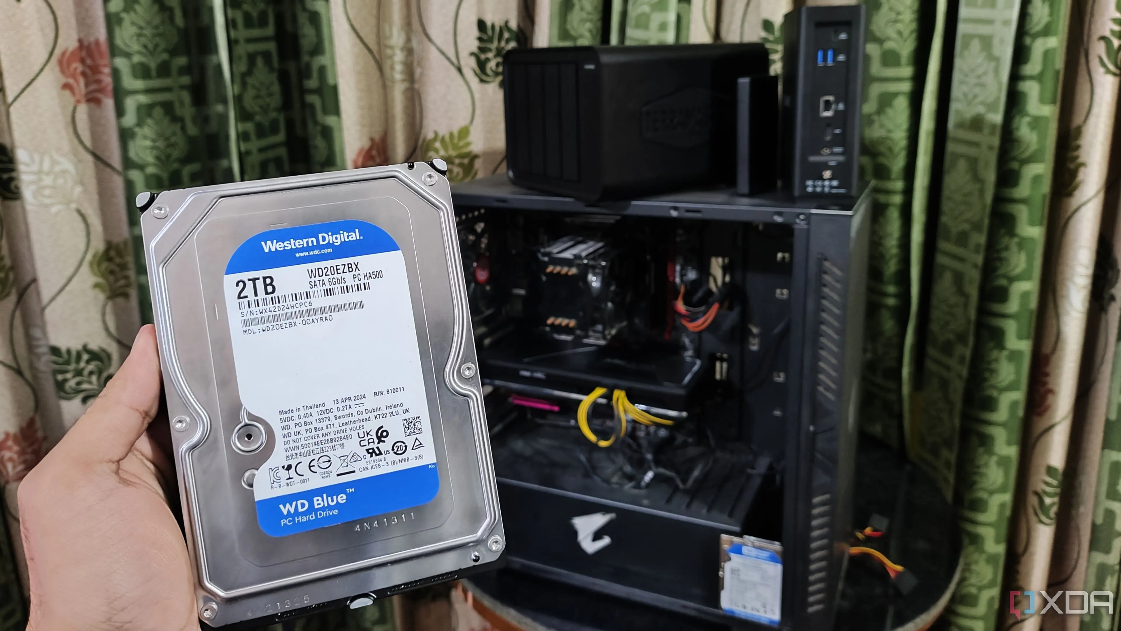 Người dùng cầm ổ cứng trước dàn PC và NAS TerraMaster, minh họa vấn đề thiếu khe cắm lưu trữ