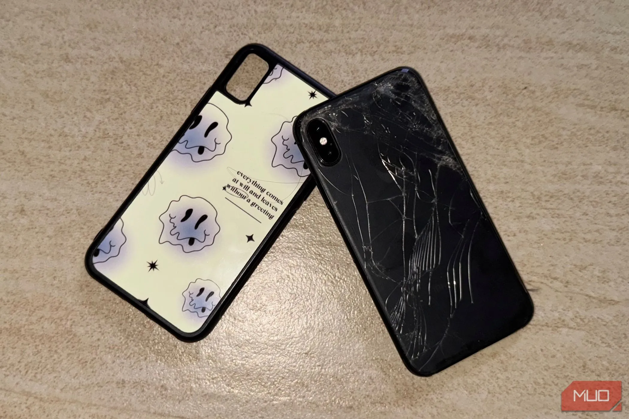 Điện thoại iPhone X bị vỡ mặt lưng kính, đặt trên sàn nhà với một chiếc ốp lưng