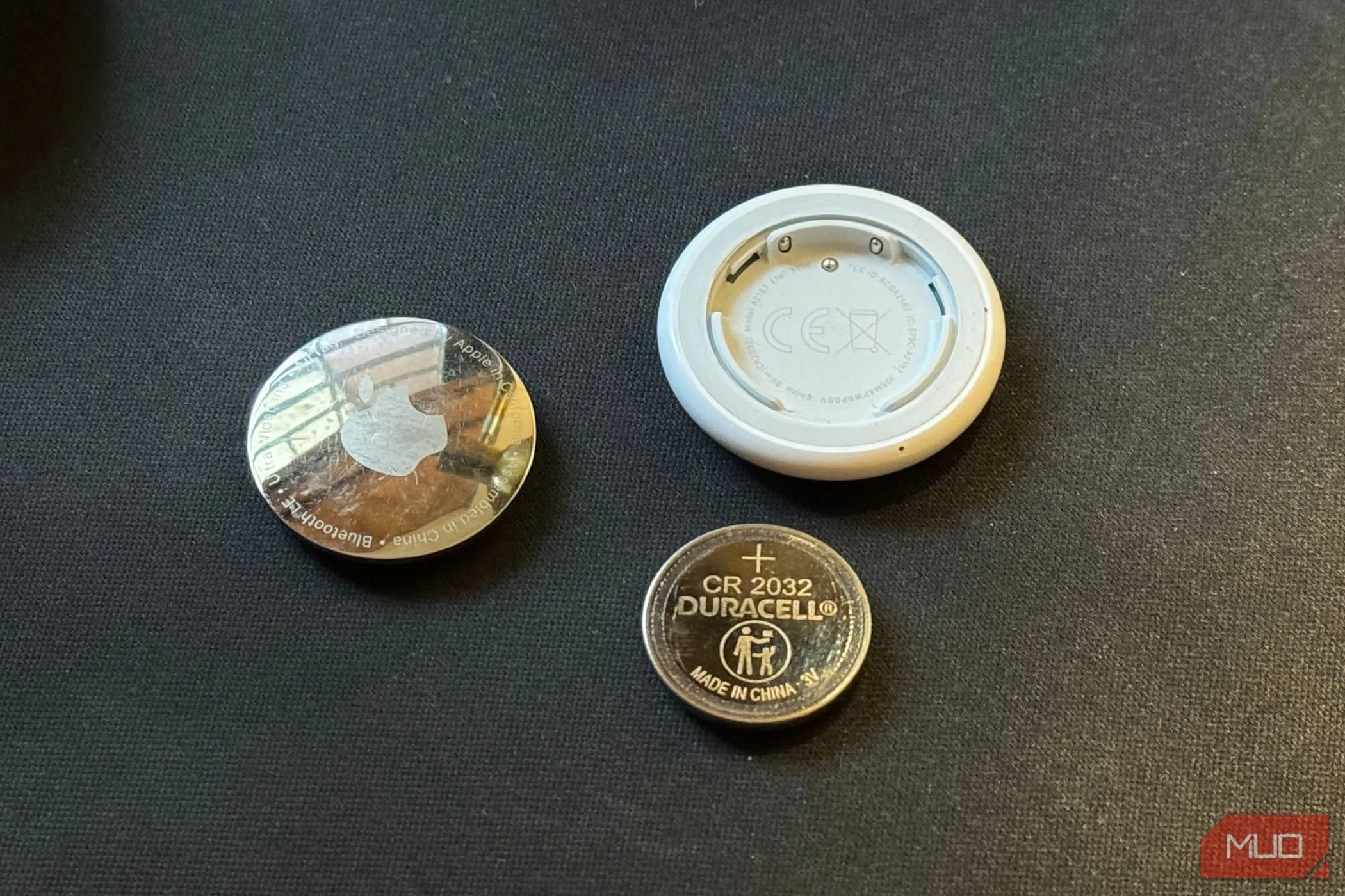 Một AirTag đã được tháo rời đặt cạnh viên pin CR 2032, cho thấy cách thay pin và quản lý thời lượng pin.