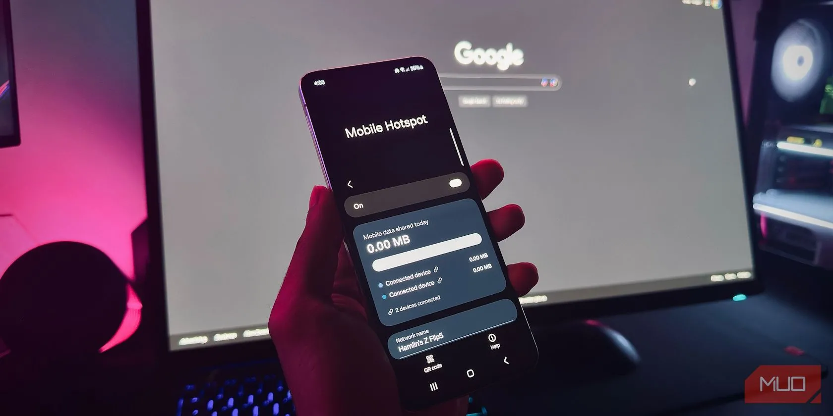 Bàn tay cầm điện thoại Android hiển thị tính năng Hotspot di động trước màn hình máy tính