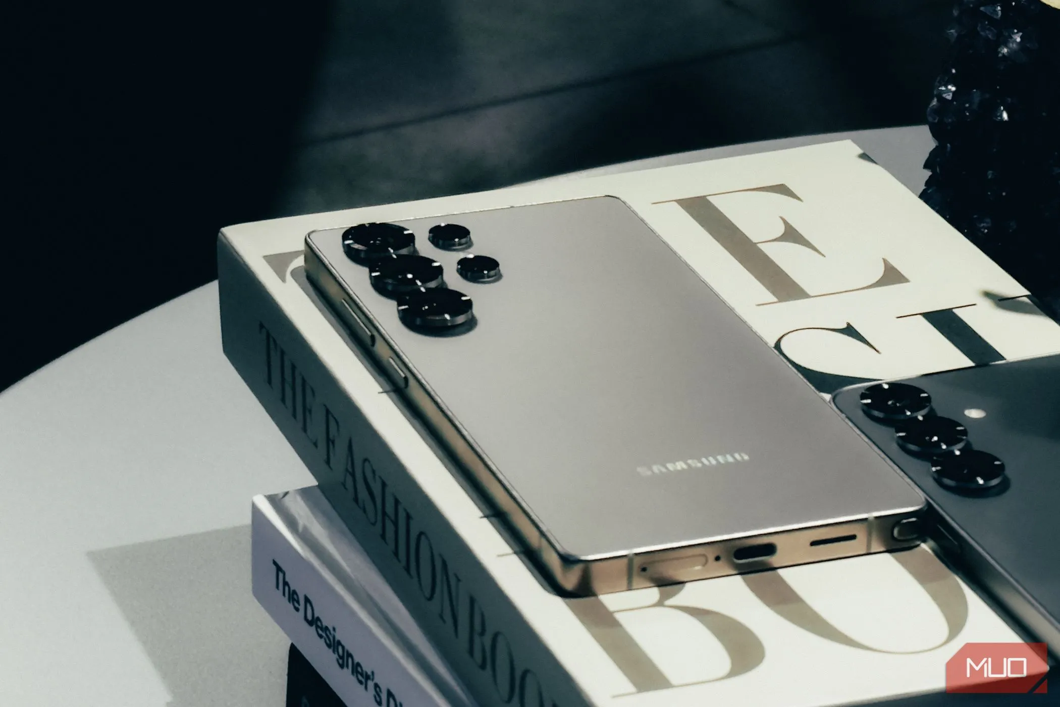 Điện thoại Samsung Galaxy S25 màu bạc đặt nghiêng trên sách, minh họa thiết kế sang trọng nhưng thiếu nam châm tích hợp cho sạc không dây Qi2.