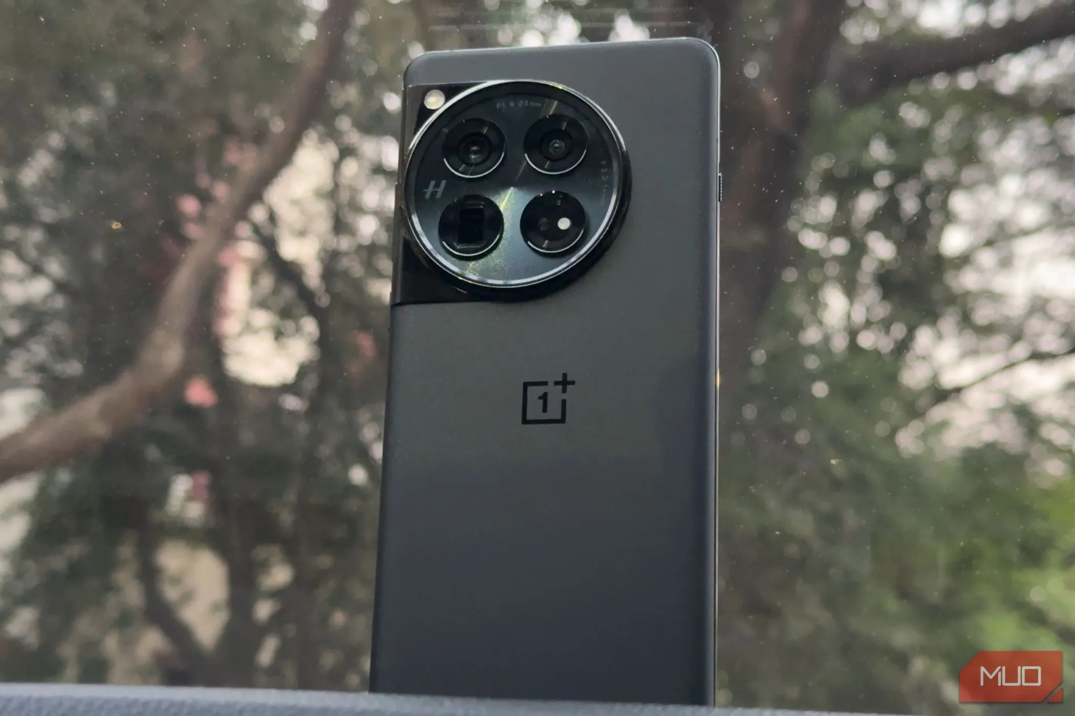 Hình ảnh điện thoại OnePlus 12 màu đen với mặt lưng kính bóng bẩy, đặt trên bảng điều khiển ô tô, thể hiện vẻ ngoài cao cấp và sang trọng của thiết bị.