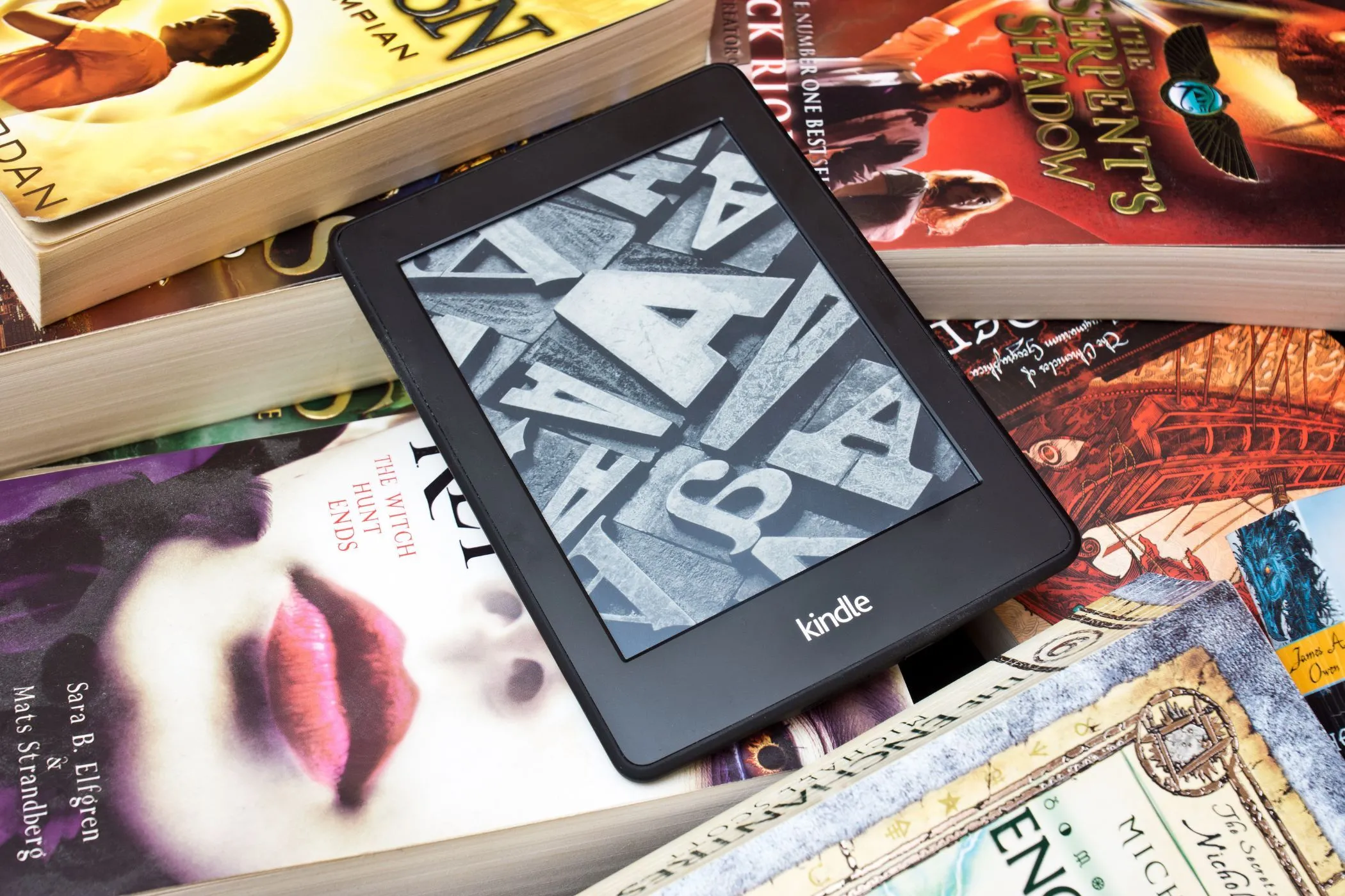 Máy đọc sách Kindle nằm trên chồng sách vật lý, biểu tượng cho sự thay đổi trong cách quản lý thư viện sách điện tử.