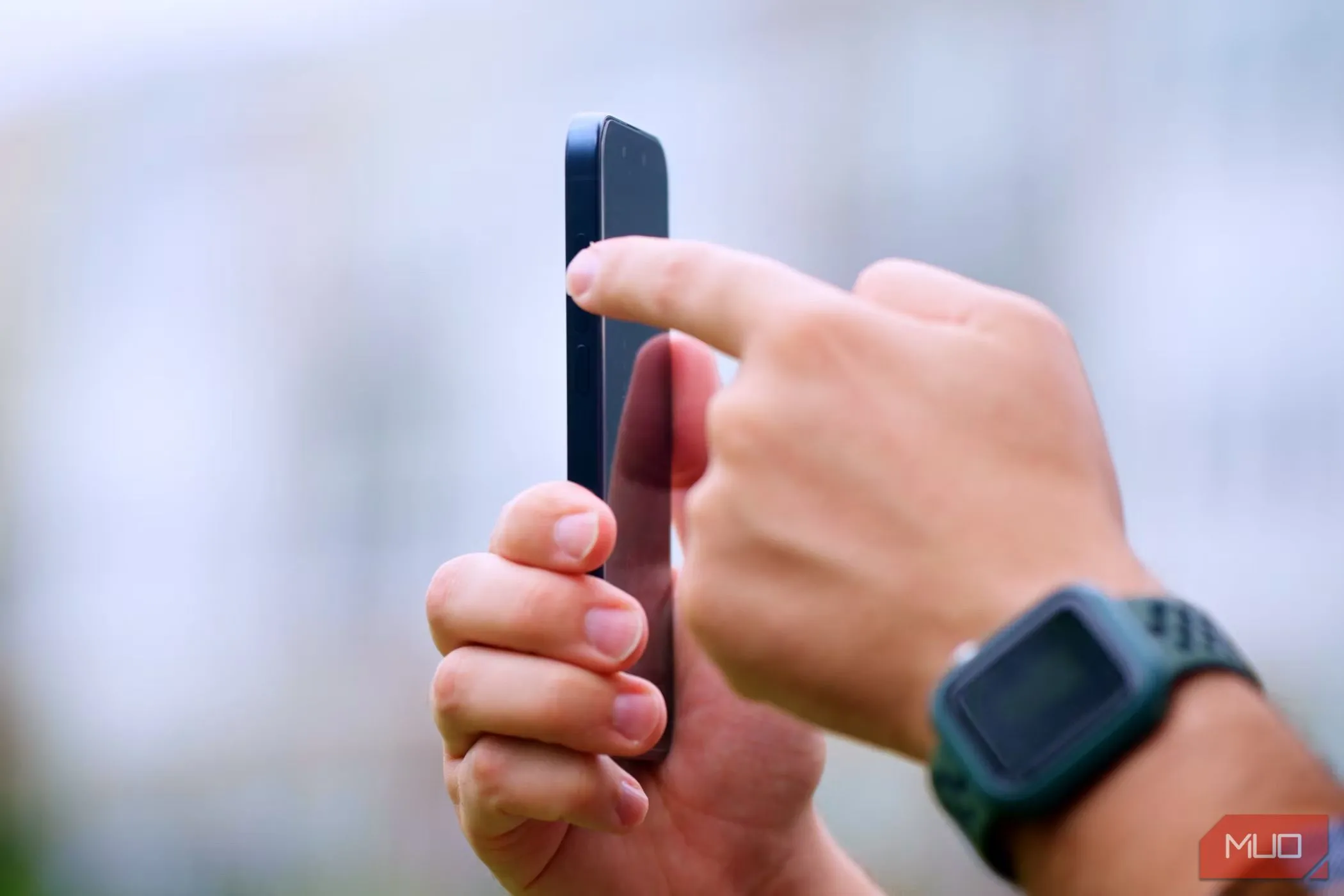 Người đàn ông cầm iPhone 15 Pro trong tay phải, ngón trỏ trái đang nhấn nút Tác vụ ở cạnh bên