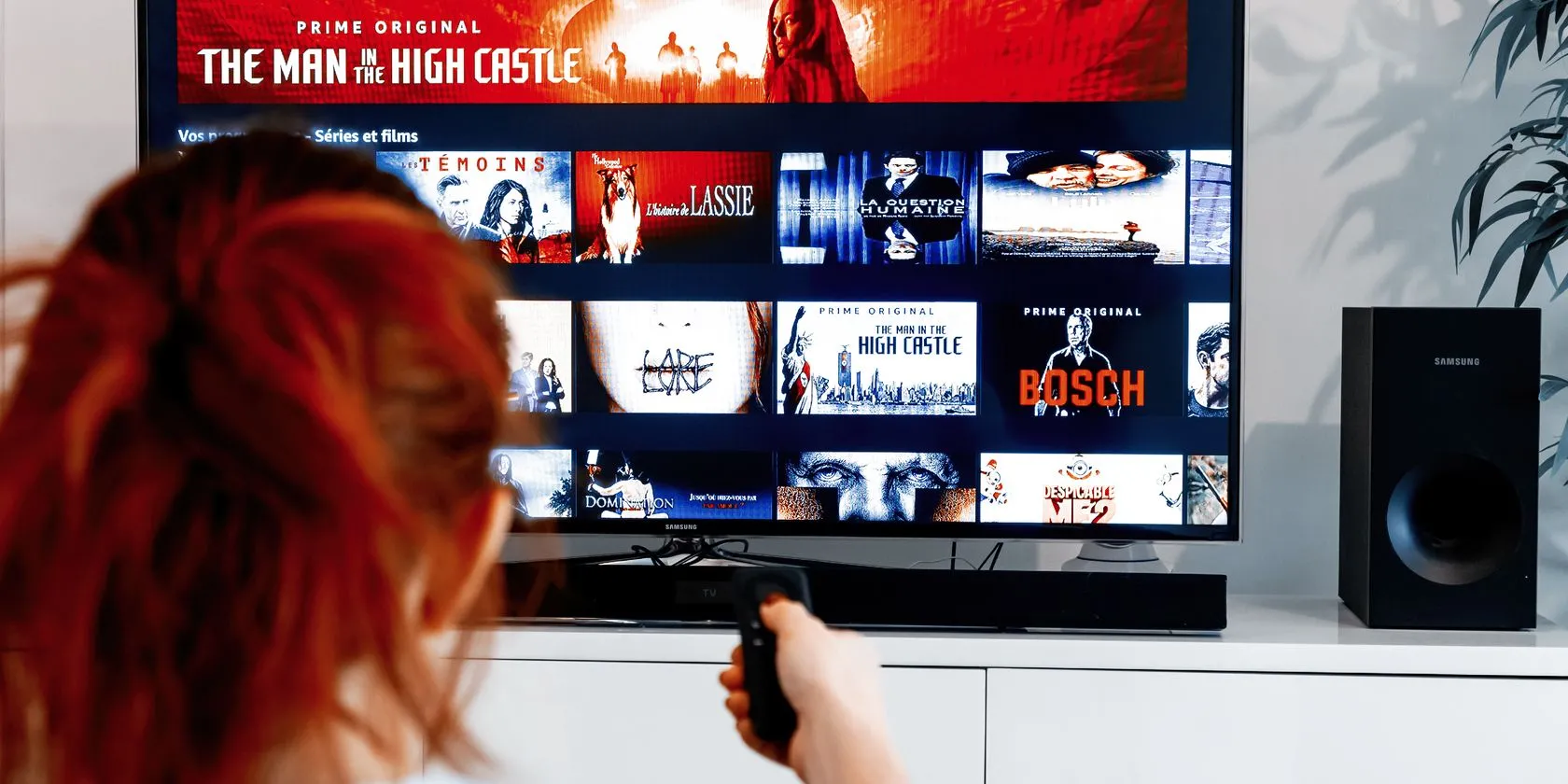 Người phụ nữ đang dùng điều khiển TV với giao diện Amazon Prime Video hiển thị trên màn hình, tượng trưng cho trải nghiệm xem phim cá nhân hoặc tính năng Watch Party trước đây.