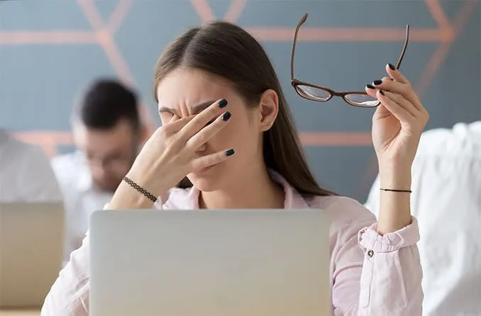 Người phụ nữ trẻ dụi mắt vì căng thẳng mắt kỹ thuật số do sử dụng màn hình điện thoại, máy tính